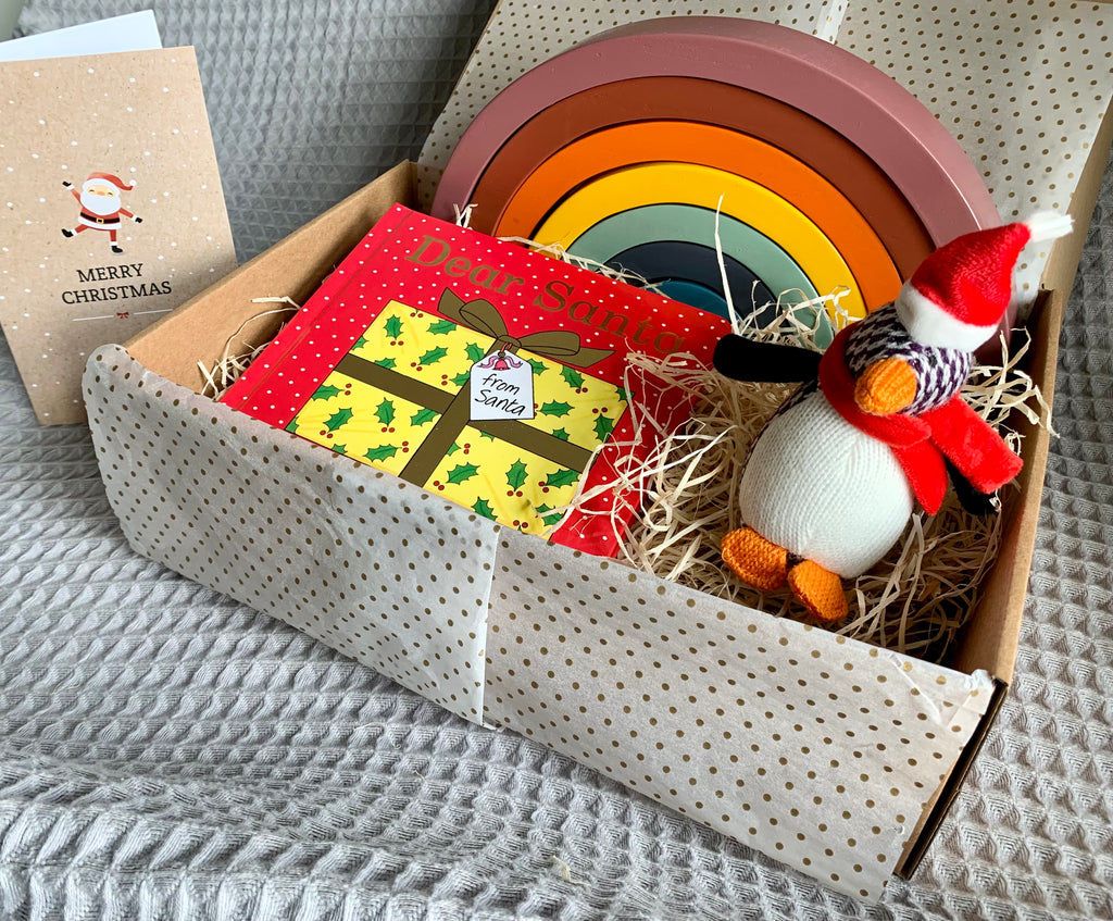 Christmas gift box in bright colours with wooden toy rainbow, dear santa book and penguin christmas decoration
